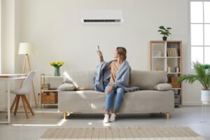Woman who is sitting on a sofa, wrapped in a warm gray blanket as she tries to get her AC to work